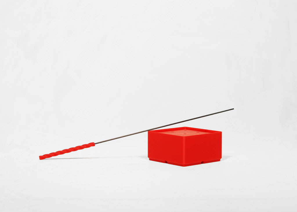 A long black rod with a bright red textured handle resting diagonally across a small red cube on a light gray background.
